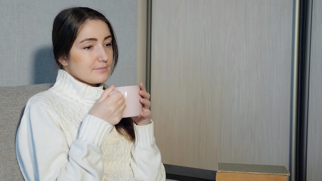 Hermosa chica bebiendo té y leyendo un libro en el sofá, cerrar