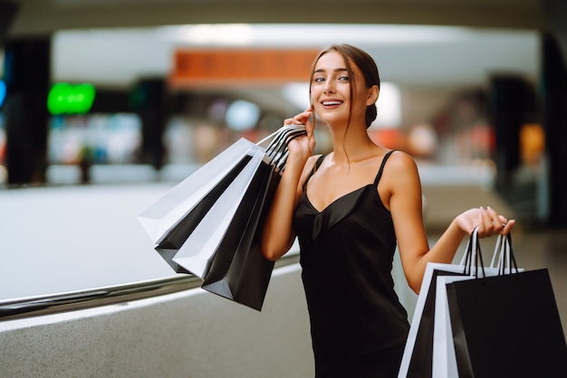 Hermosa chica con bolsas de compras mirando a la cámara y sonriendo mientras hace compras en el centro comercial