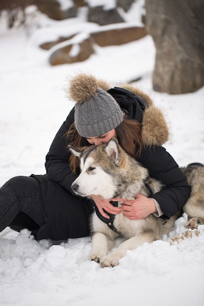 Hermosa chica en bosque de invierno con perro. Juega con el perro husky siberiano.