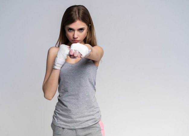 Hermosa chica boxeadora con guantes y ropa deportiva practicando en el estudio sobre gris.