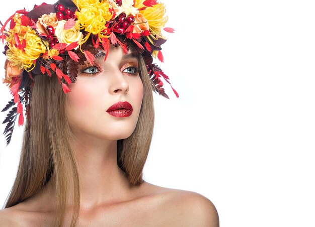 Hermosa chica con brillante corona otoñal de hojas y flores Cara de belleza Foto tomada en el estudio sobre un fondo blanco