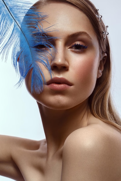 Hermosa chica bronceada con maquillaje creativo y plumas de pestañas azules en la mano Cara de belleza