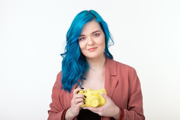 Hermosa chica con cabello azul sostenga la cámara retro amarilla en la pared blanca