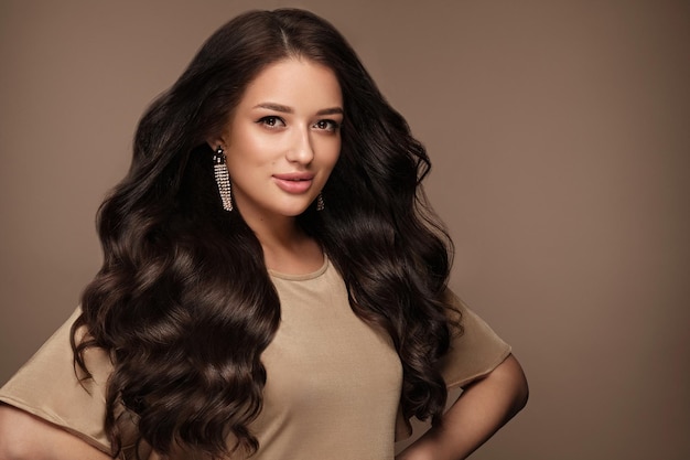 Hermosa chica de cabello castaño con un cabello perfectamente rizado y maquillaje clásico Cara y cabello de belleza Foto tomada en el estudio