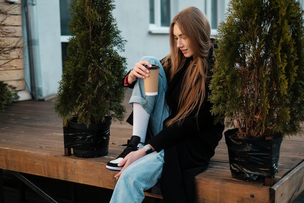 Una hermosa chica con cabello largo con café sentada en un banco y mirando hacia otro lado