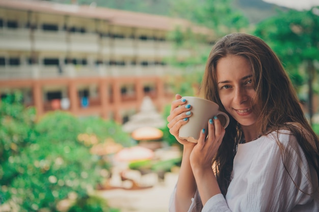 Hermosa chica con cabello largo y manicura azul sosteniendo una taza grande