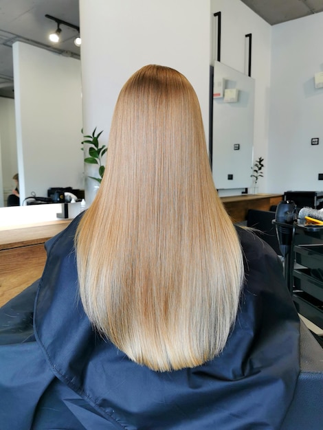 Hermosa chica de cabello largo y rubio en un salón de belleza después del cuidado del cabello Vista desde atrás Peluquería