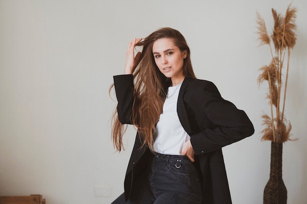 Hermosa chica con cabello largo se sienta en una silla en una hermosa habitación escandinava y posa para una foto