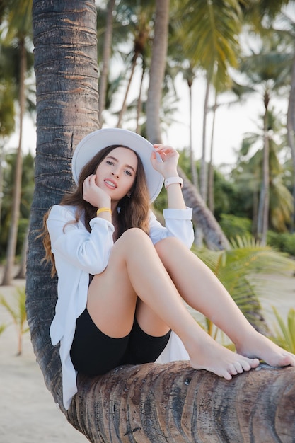 Hermosa chica de cabello oscuro feliz europea cerca de la palma de coco en la playa de arena blanca