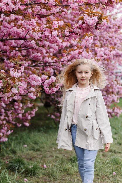 Hermosa chica camina cerca de las ramas florecientes de sakura japonesa