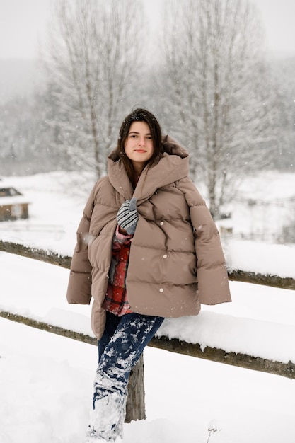 Hermosa chica camina en una nevada. Mujer joven divirtiéndose en el bosque de invierno.Retrato al aire libre de dama bonita morena posando en madera