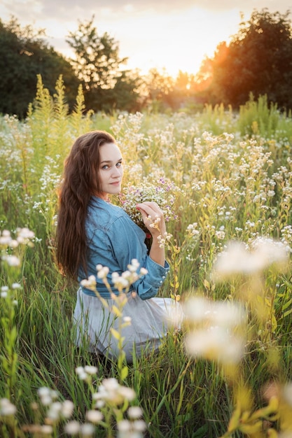 Hermosa chica caminando en el campo en verano con flores silvestres