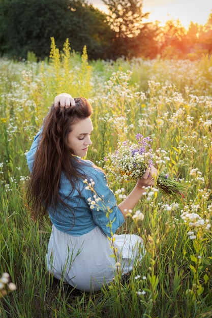 Hermosa chica caminando en el campo en verano con flores silvestres