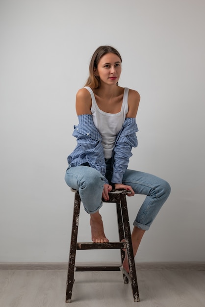 Hermosa chica en una camiseta blanca, jeans azul sentado en una silla, sonriendo y posando