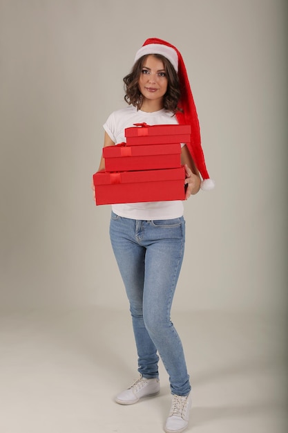 Hermosa chica en una camiseta blanca con un sombrero de Santa Claus tiene cajas de regalo rojas en sus manos