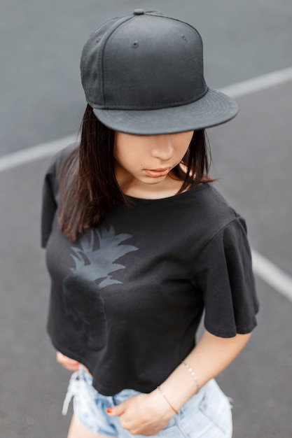 Foto hermosa chica en camiseta negra estilo botín y una gorra en el estadio.