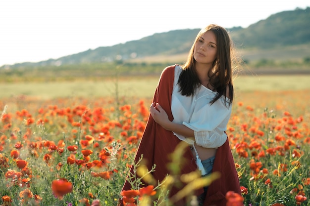 Hermosa chica en un campo de amapolas al atardecer. concepto de libertad