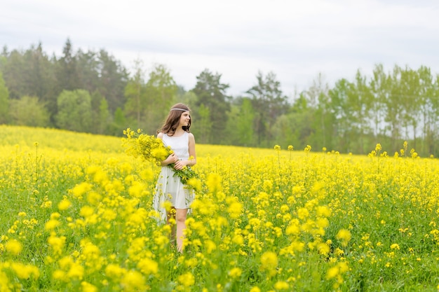 Hermosa chica en un campo de colza. Un niño en un campo floreciente con flores amarillas. Plantación de flores amarillas