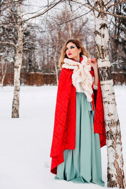 Hermosa chica en una capa roja en el bosque de invierno