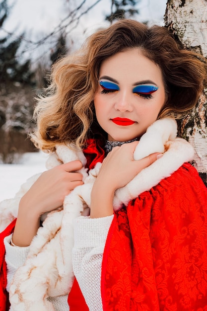 Hermosa chica en una capa roja en el bosque de invierno