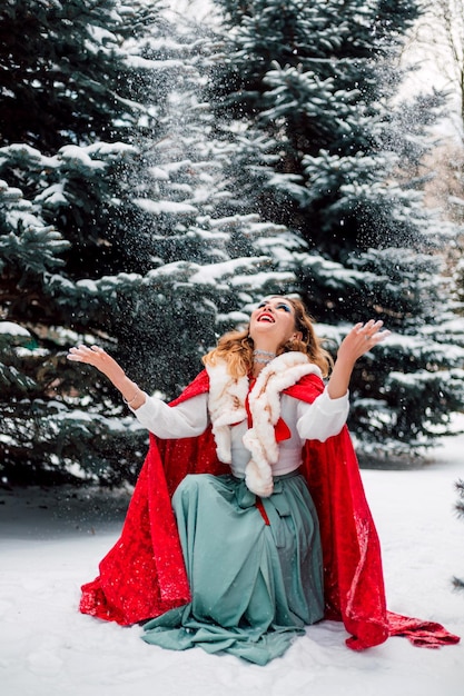 Hermosa chica en una capa roja en el bosque de invierno