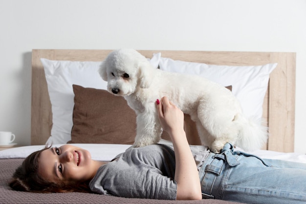 Hermosa chica en casa con un perro La anfitriona con un bichón juega en la cama