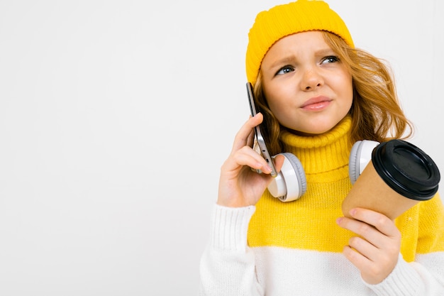 Hermosa chica caucásica adolescente con sombrero amarillo, pantalón, camiseta blanca y chaqueta tiene una mochila grande en sus manos aisladas en blanco