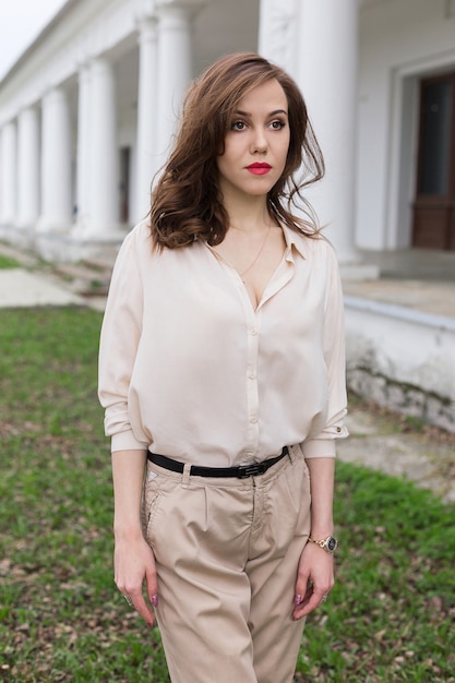 Foto hermosa chica caucásica con labios rojos, cabello rizado en elegante blusa beige mira cuidadosamente a un lado. concepto de soledad