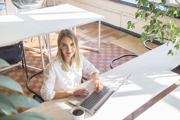 Hermosa chica caucásica trabajando en una computadora portátil de forma remota en un interior brillante.