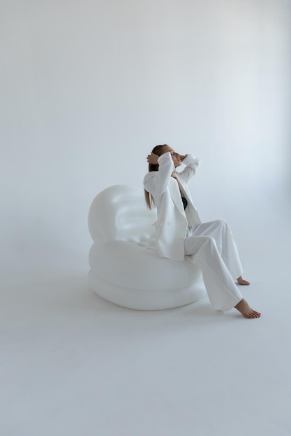 Hermosa chica caucásica en un traje blanco se sienta en una pose de moda en el estudio sobre un fondo blanco.