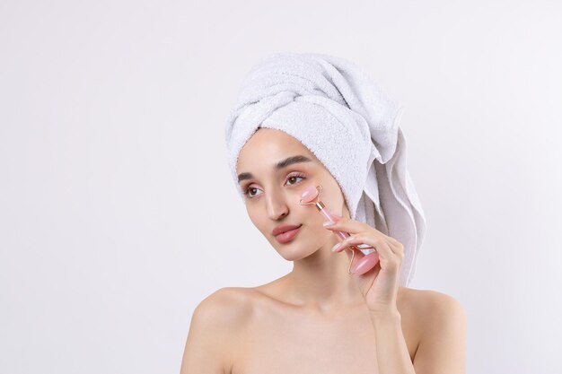 Hermosa chica con cejas gruesas y piel perfecta en una toalla de fondo blanco en la foto de belleza de la cabeza Sostiene un rodillo cosmético