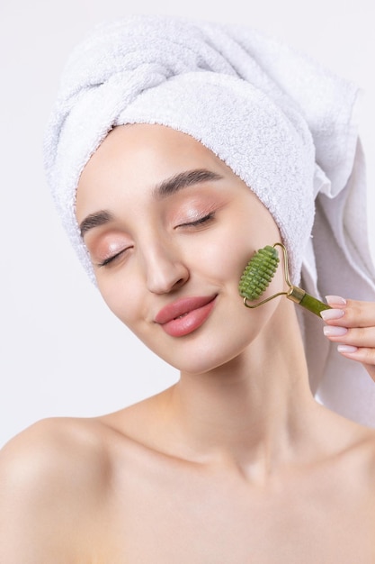 Hermosa chica con cejas gruesas y piel perfecta en una toalla de fondo blanco en la foto de belleza de la cabeza Sostiene un rodillo cosmético