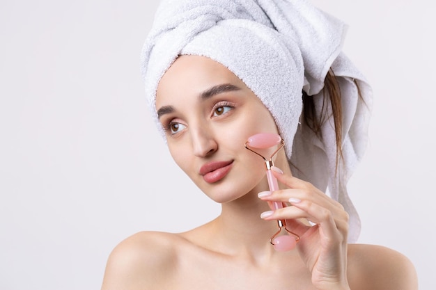 Hermosa chica con cejas gruesas y piel perfecta en una toalla de fondo blanco en la foto de belleza de la cabeza Sostiene un rodillo cosmético