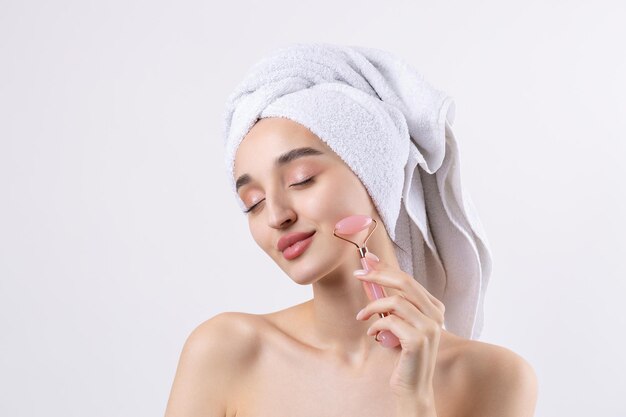 Hermosa chica con cejas gruesas y piel perfecta en una toalla de fondo blanco en la foto de belleza de la cabeza Sostiene un rodillo cosmético