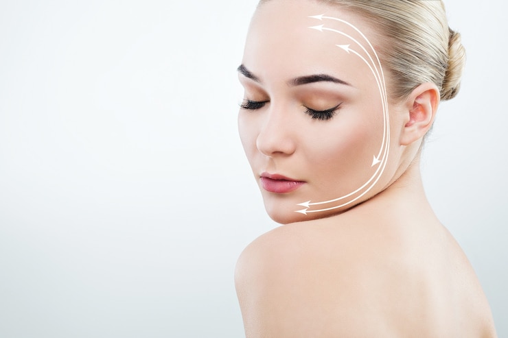 Foto hermosa chica con cejas oscuras y cabello castaño sosteniendo el hombro desnudo cerca de la cara, mirando hacia abajo, modelo con maquillaje desnudo claro, fondo de estudio blanco, foto de belleza.