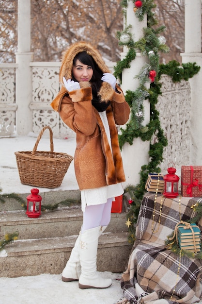 Hermosa chica en un cenador decorado de Navidad con un abrigo de piel de oveja