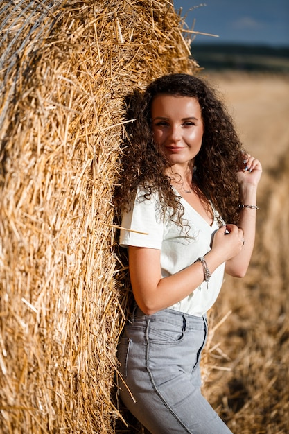 Hermosa chica cerca de fardos de heno en el campo. Chica en el fondo de un pajar