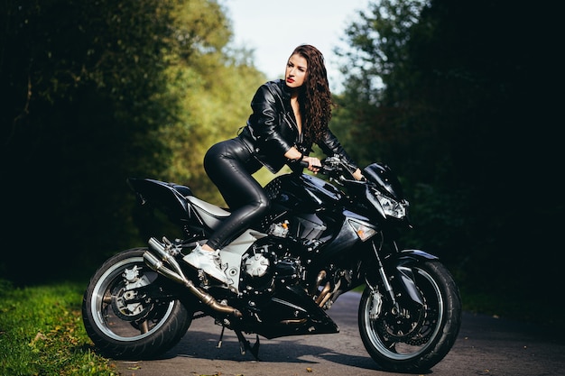 hermosa chica cerca de la motocicleta negra, retrato, en el bosque cerca de la carretera, otoño