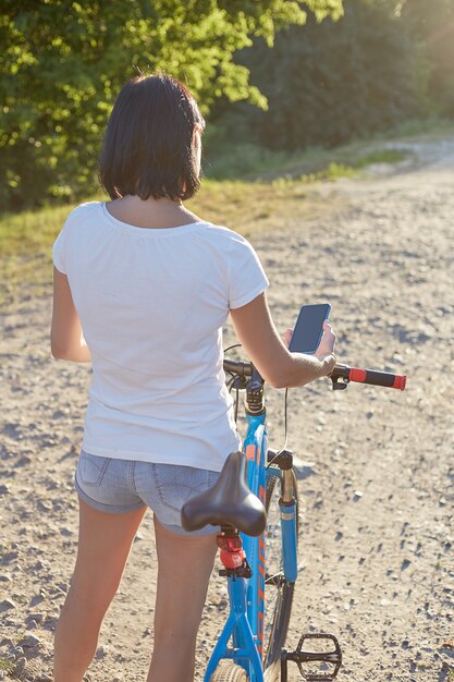 Hermosa chica ciclista con una bicicleta en el camino hacia la puesta del sol. Hobbies y deportes.