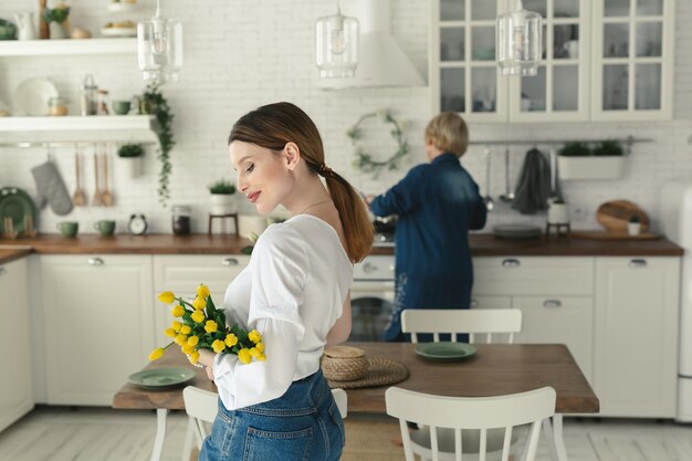 Hermosa chica se para en la cocina y sostiene tulipanes en sus manos Día de la Mujer 8 de marzo