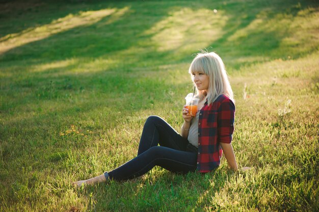 Hermosa chica con un cóctel de naranja sobre la hierba en el parque