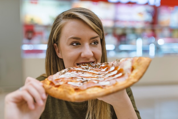 Hermosa chica comiendo sabrosa pizza sobre fondo claro.