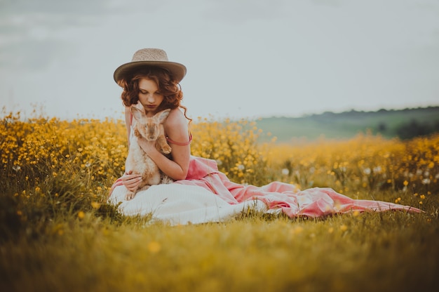 Hermosa chica con un conejo al aire libre en día de verano