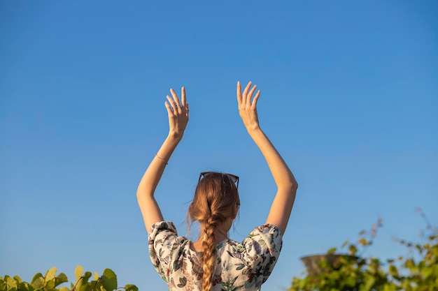 Foto hermosa chica contra el cielo. brazos levantados ligeramente por encima de la cabeza contra el cielo. femenino suave