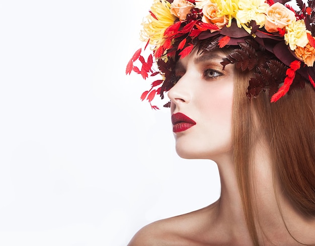 Hermosa chica con corona de otoño brillante de hojas y flores Cara de belleza