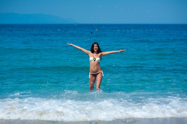 Hermosa chica con cuerpo perfecto en bikini traje de baño jugando con agua en la playa de las Maldivas