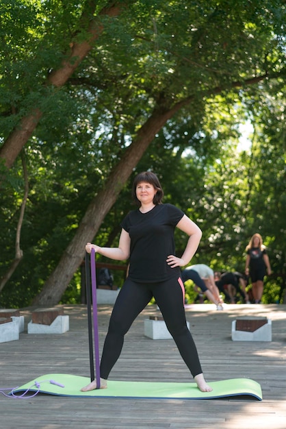 Hermosa chica se dedica a fitness en el parque. Banda elástica para fitness. La mujer realiza ejercicios para bombear los brazos.