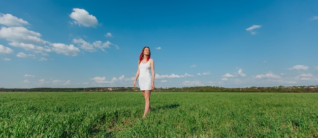 Hermosa chica delgada caminando sobre un panorama de campo verde