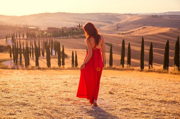 Hermosa chica delgada con un vestido rojo al atardecer en la Toscana, Italia