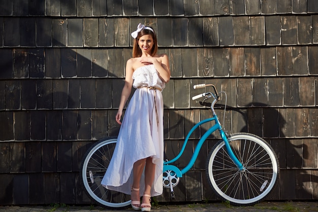 Hermosa chica en un día soleado contra bicicleta vintage y pared
